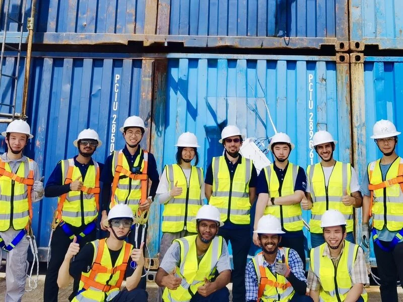 The MARMoT Laboratory team in hard hats and high-visibility vests, posing in front of shipping containers