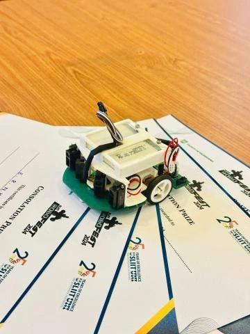 Team Quanta's micromouse, a compact green PCB robot with side-facing IR sensors, resting on Robofest 2024 certificates