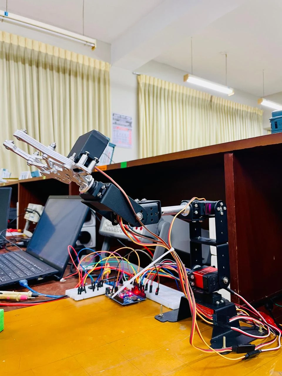 5-DOF servo robot arm with a metal gripper, wired to an Arduino on a lab bench